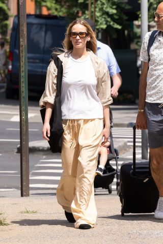 Jennifer Lawrence wearing a white tee, beige button-down, butter yellow parachute pants, and maxi black tote bag while out in New York City June 2024