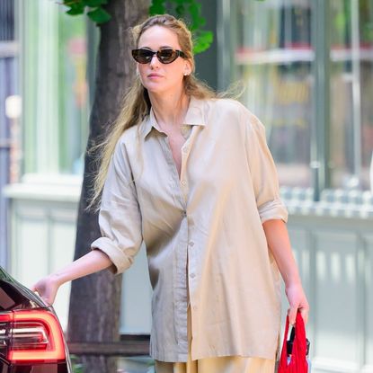 Jennifer Lawrence gets into her car wearing a beige shacket and butter yellow pants plus white sneakers